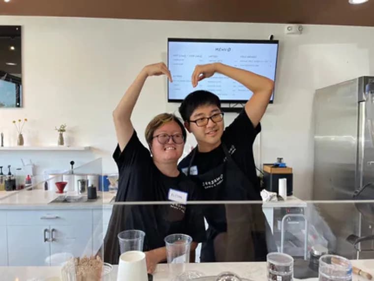Two Seesaw baristas smiling and making a heart shape with their hands.