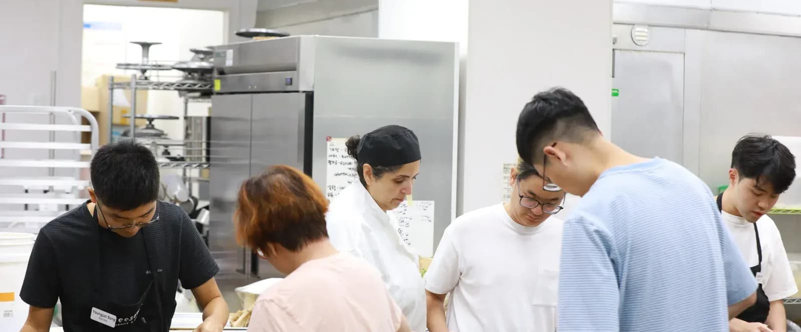 A group of trainees and an instructor working together at a stainless-steel baking kitchen.