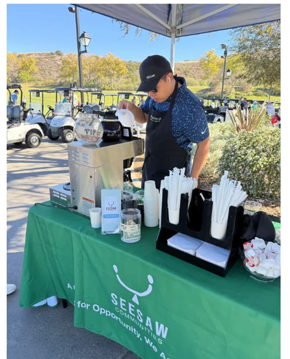 A Seesaw barista serving fresh coffee from the cart at a bright outdoor event.