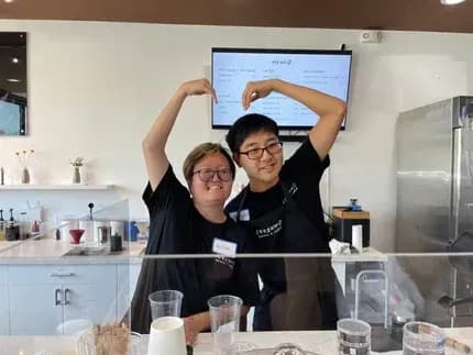Two Seesaw team members making a heart shape behind the cafe counter.