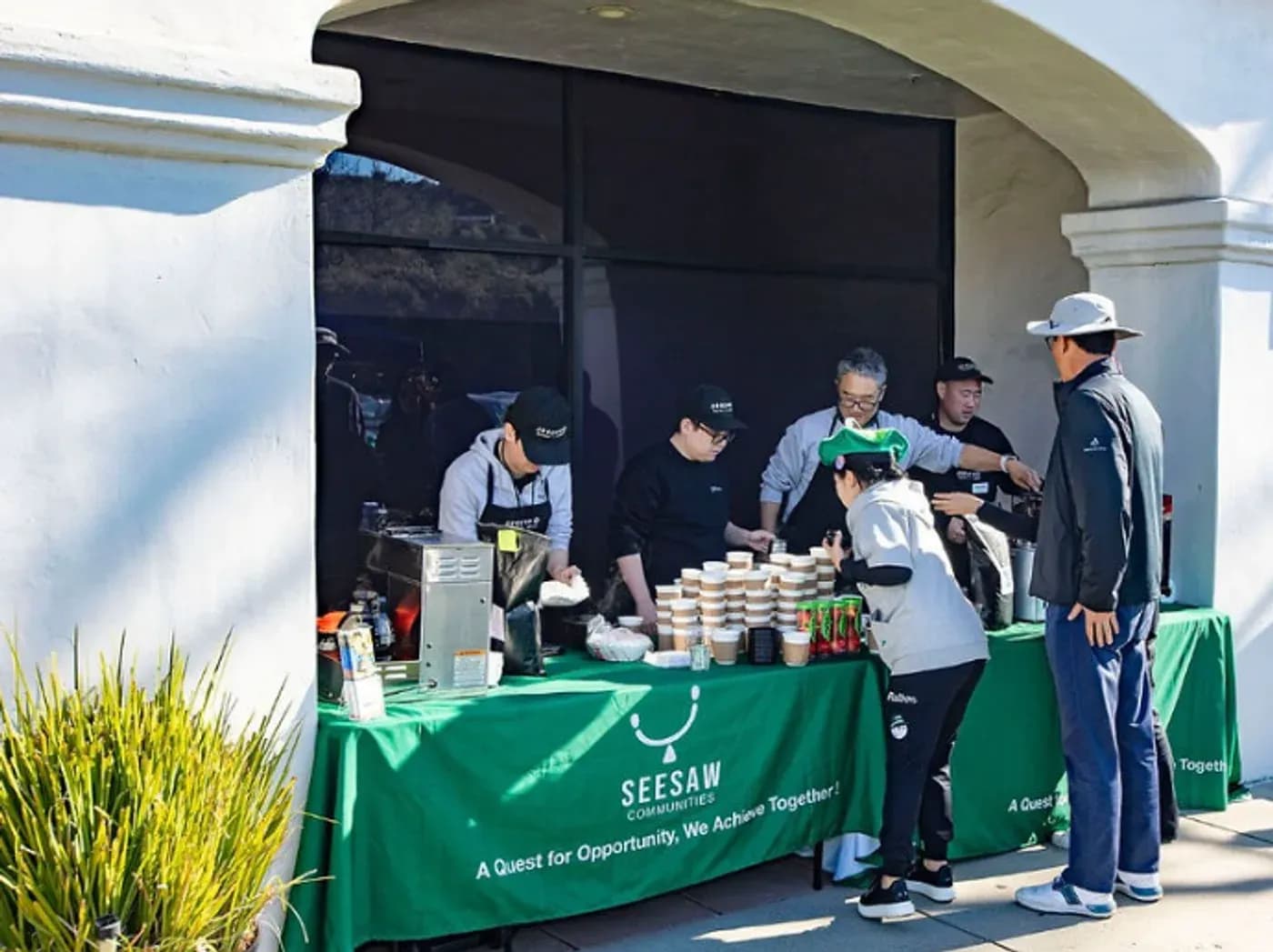 Seesaw participants in green aprons serving coffee at a community event from the Seesaw coffee cart.