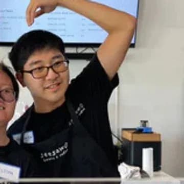 Youngjun, a Seesaw barista, smiling with his arm raised.